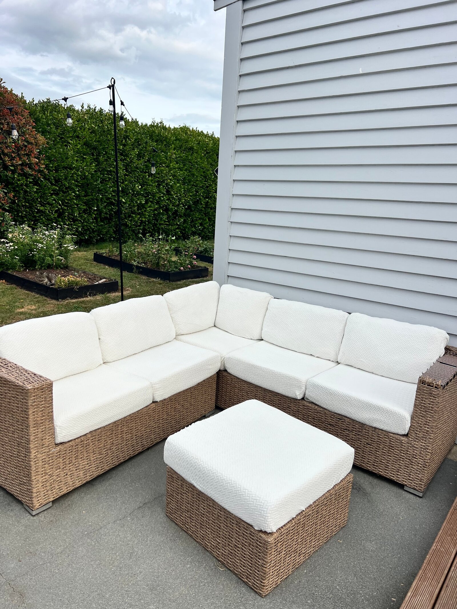 After: the wicker corner lounge and ottoman with clean white textured covers in front of the garden beds